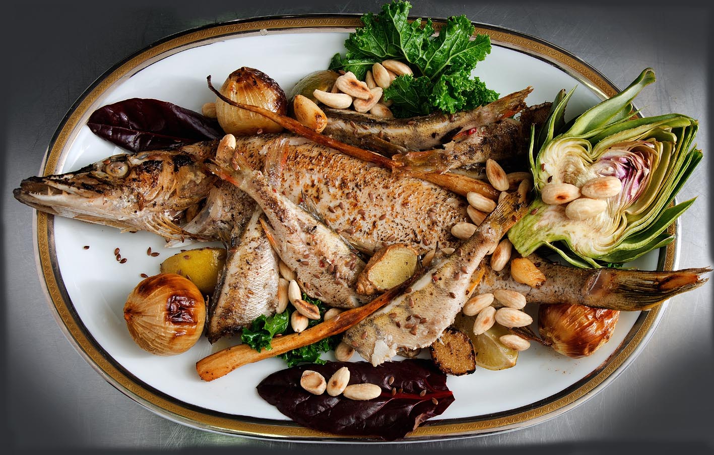 Zdjęcie smakowitej potrawy. Przedstawia rybę przyozdobioną warzywami i orzechami. 