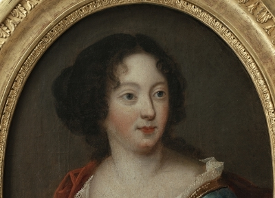 Fragment portretu olejnego młodej kobiety. Kobieta ma ciemne włosy spięte do tyłu, pogodną twarz, duże oczy i lekki uśmiech na twarzy. Ubrana jest suknię z dekoltem i czerwony płaszcz. Jest to fragment portretu Teresy Kunegundy Sobieskiej. 