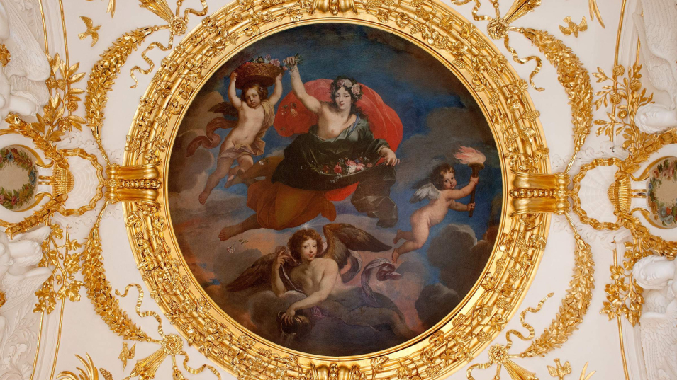 Okrągłe malowidło w złotej ramie na tle białego sufitu ze złoconymi elementami.