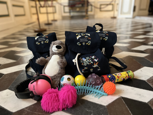 Szmaciany plecak z napisem: Sensorium Wilanowskie, wokół zabawki.