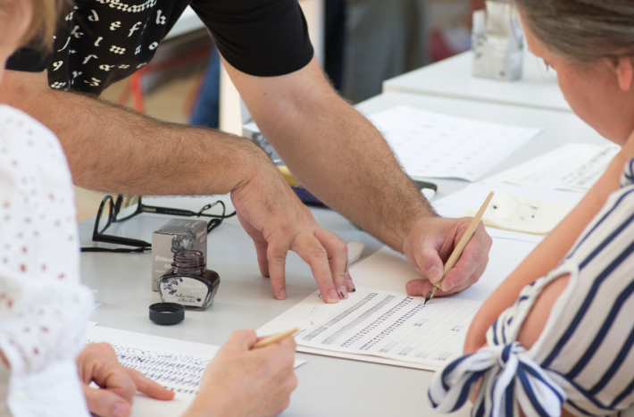 Mężczyzna uczy dwie kobiety kaligrafii - odręcznego pięknego pisma.