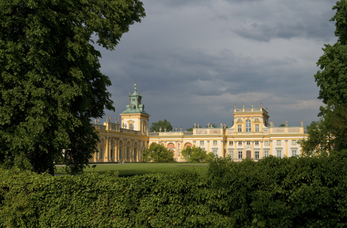 Zdjęcie przedstawia pałac wilanowski w otoczeniu krzewów i drzew.